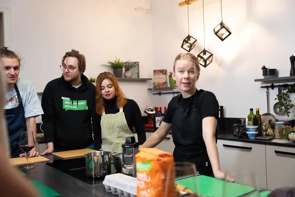 Элина рассказывает группе взрослых у кухонного стола